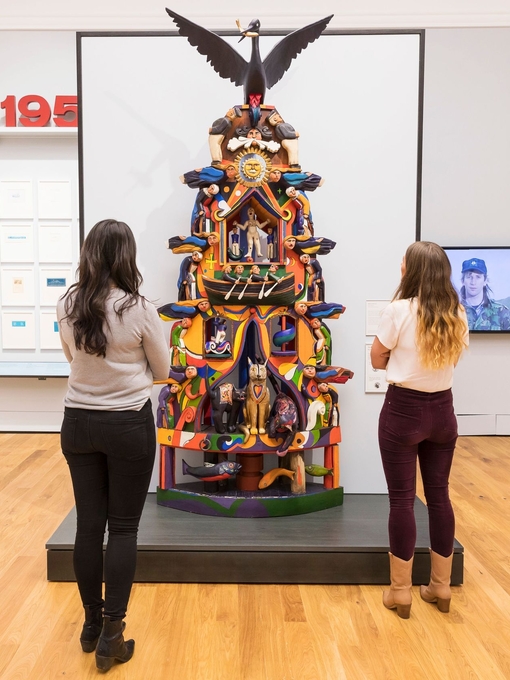 People admiring a sculpture of a totem pole in an art gallery.