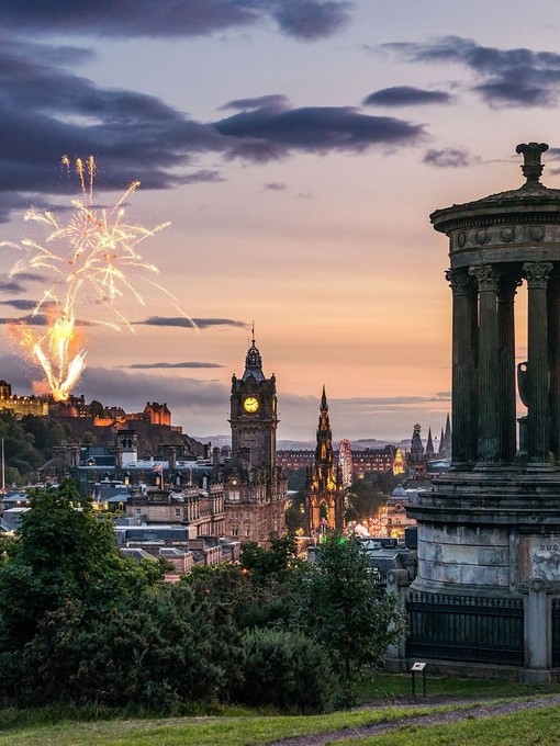 Fireworks at dusk in the sky over historic city monuments and castle.