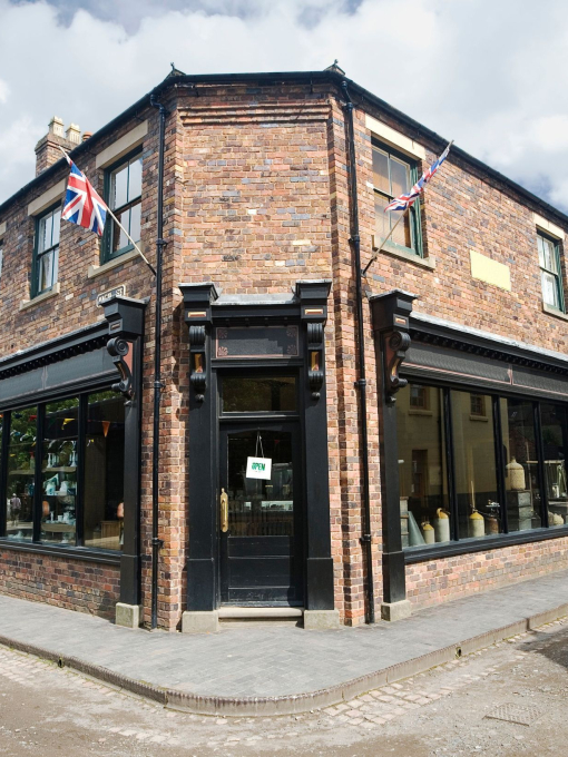 View of a Victorian corner shop with large windows and Union Jack flags mounted on the facade