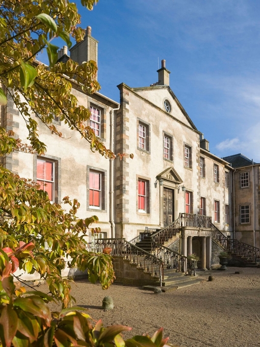 Exterior of a light-brick stately home with staircase entrance, framed by foliage.