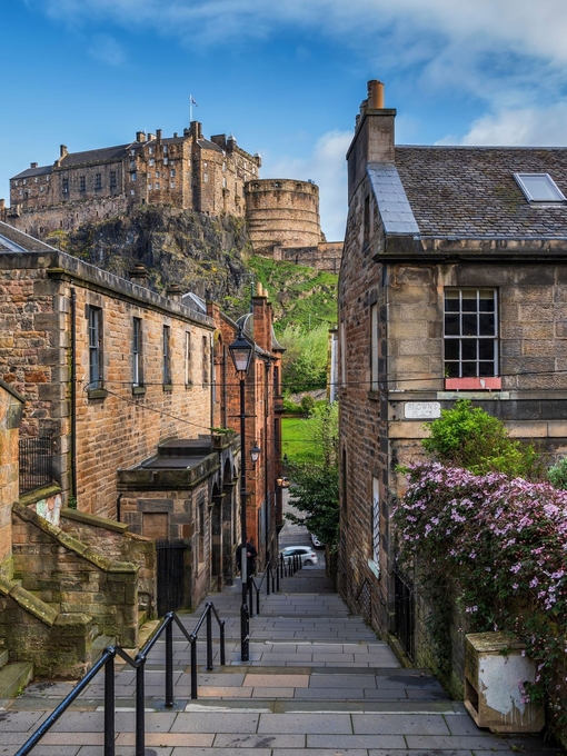 Narrow alley steps going down between two houses with a castle in the background