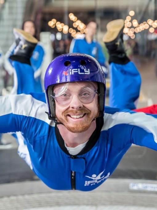 Una persona che fa un'esperienza di iFLY Indoor Skydiving con una folla di persone che guarda dietro di sé
