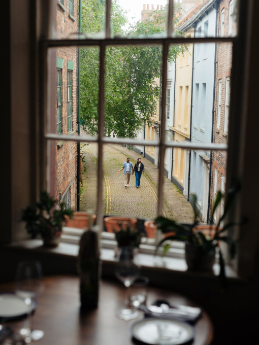 A man and a woman walk along a cobbled street seen through a window