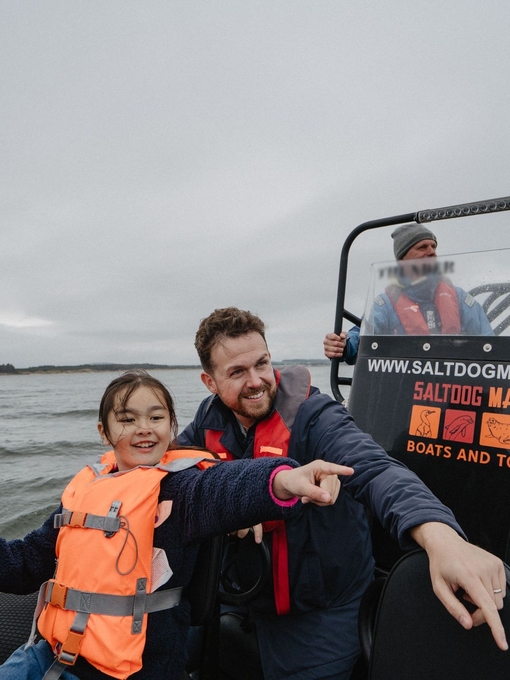 A man and a girl point at something from inside a boat with the Marine boat crew in the background.