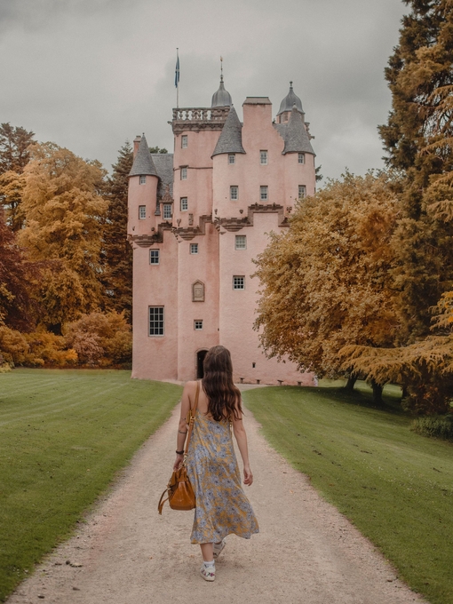 Woman walking on a path between grass, towards a castle