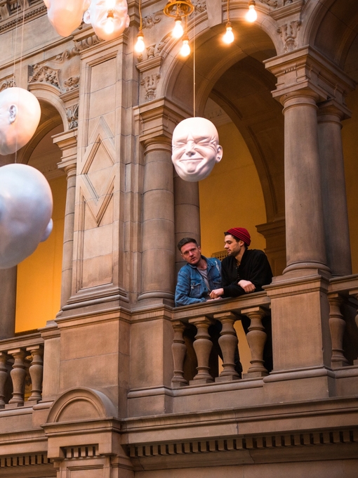 Two men looking at installation of suspended head sculptures