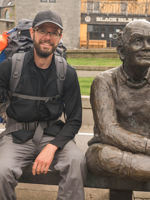 A man with walking sticks posing next to a statue on a bench in Glasgow