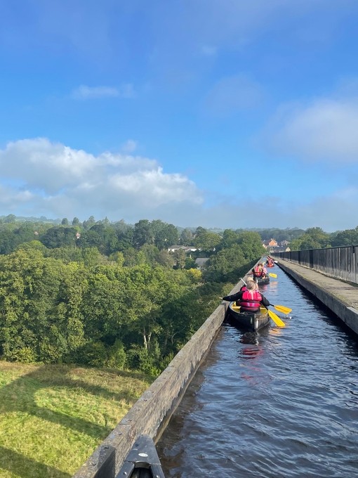 A group paddling kayaks across a viaduct with scenic views of Snowdonia/Eryri National Park