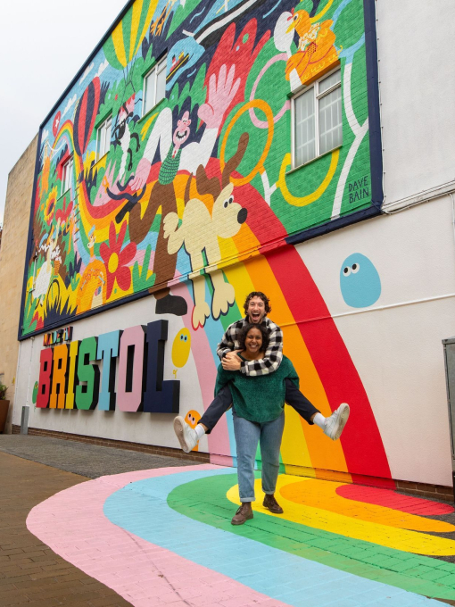 Two people playfully smiling and posing in front of a colourful mural