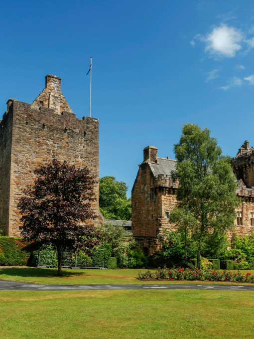 Exterior of a small castle with a flagpole and a few trees on a sunny day.