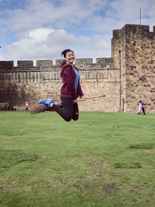 Young woman hovering on a broomstick in the Outer Bailey of Alnwick Castle
