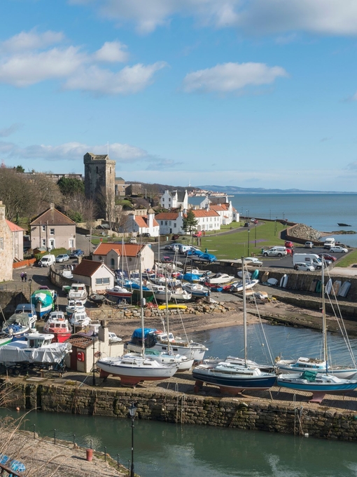A small harbour with small sailing yachts and a few houses on a sunny day.