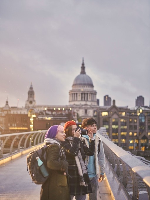 Two women and a man on a pedestrian bridge in a city taking photographs