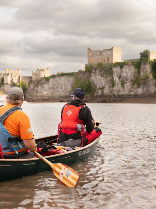 Two people canoeing along a river with a view of a castle in the background.