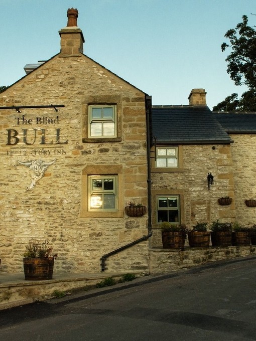 The sandy coloured stone building of a pub on the side of a road