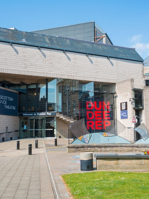 Exterior view of the Dundee Rep theatre with a person sitting outside on a bench.