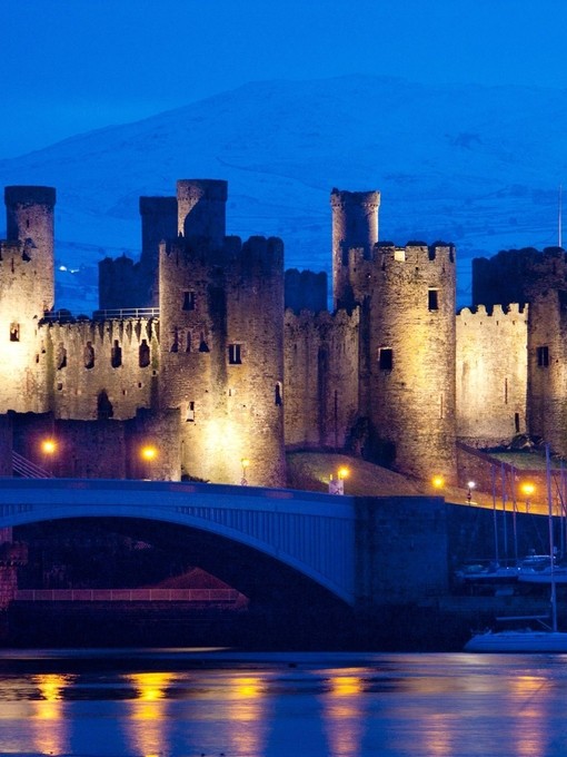 A castle lit up at night in winter snow near harbour