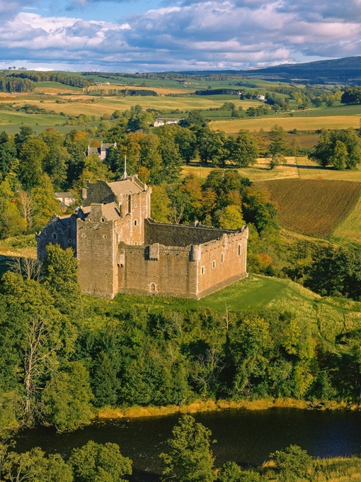 Exterior of a partly ruined medieval castle on a small hilltop overlooking fields and trees in autumn.