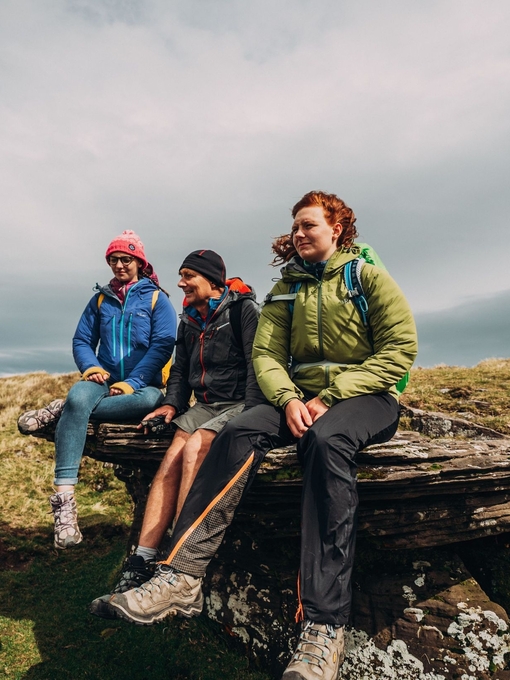 Three people sitting on a rock along a hiking route beneath a stormy sky.