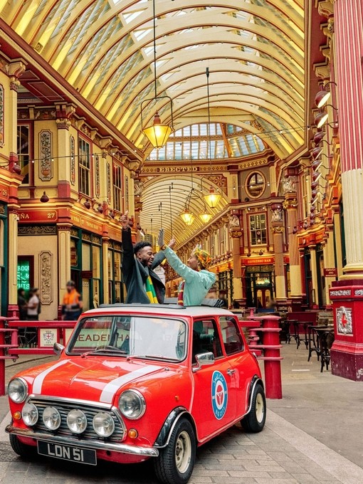 Man and woman in a vintage car under an ornate decorated gold ceiling in a market hall