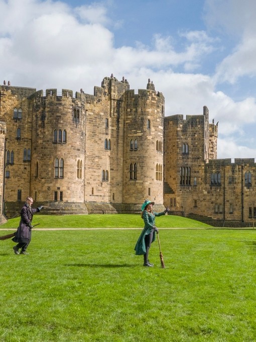 A group of people lined up for a Broomstick Training lesson with the wizarding professors by a large castle.