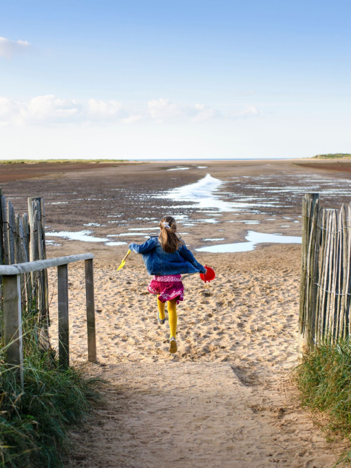 A girl running down a path to Holkham Beach
