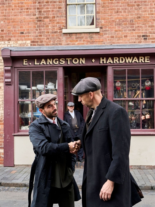 Two men shaking hands on the street in front a hardware shop at a living museum