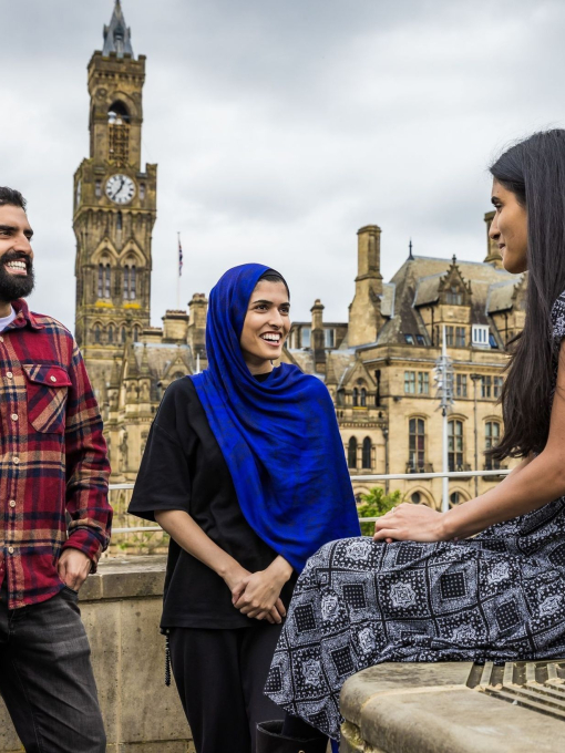 Two women and a man stand and talk in front of a town view