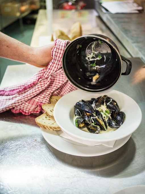 A chef plating up a bowl of mussels in a restaurant.