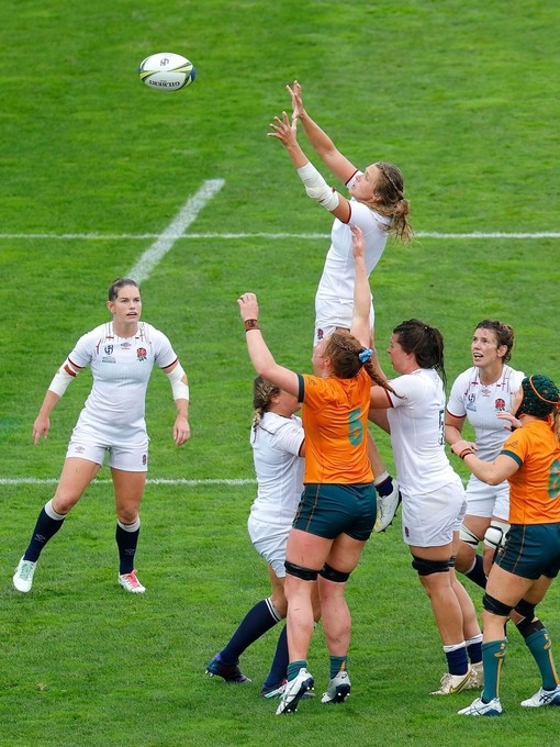 Women's rugby match with players from two teams jumping to catch the ball on the field