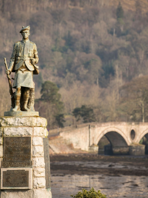 A war memorial statue in front of an arched bridge.