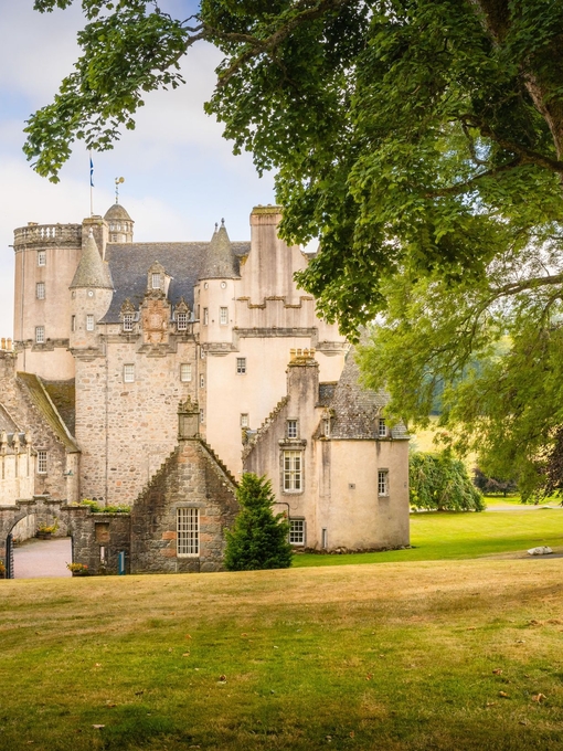 Exterior view of a Scottish castle with a large tree in front.