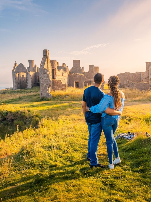 A couple enjoying the views of a castle remains at golden hour.