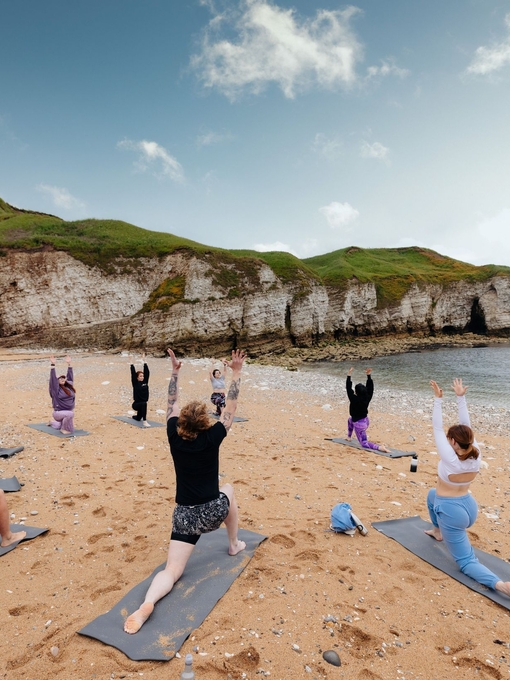 A group of people practising yoga on a beach