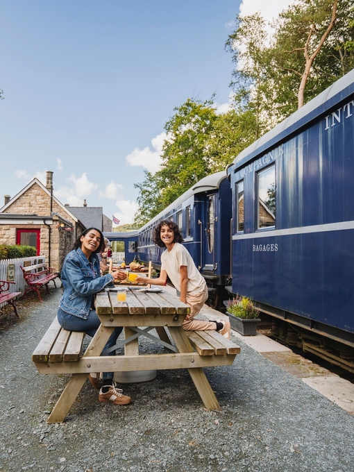 Mother and son having afternoon tea on the platform next to a heritage replica train.
