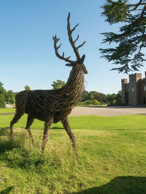 A wooden sculpture of a deer outside a castle.