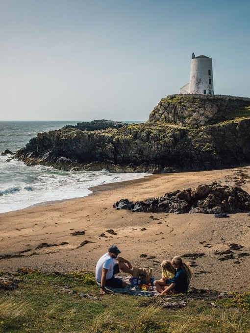 A young family picnicing on a beach with a lighthouse in the background.