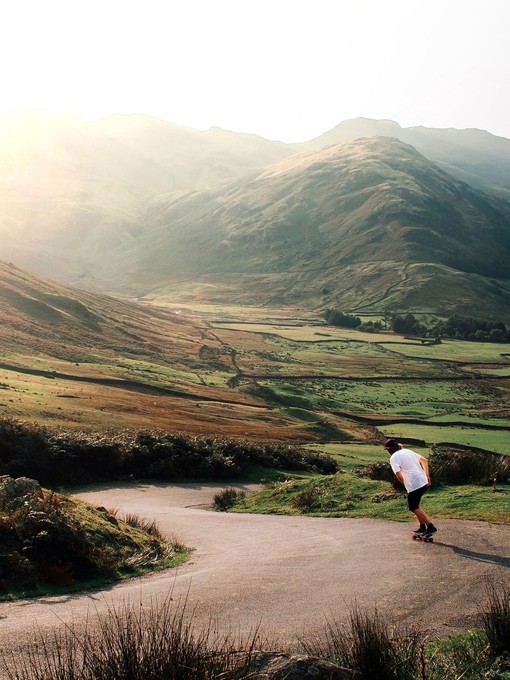 Man skateboarding down valley paths. Green landscape