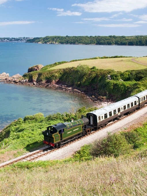 Steam train on railway line along coastline. Sea views