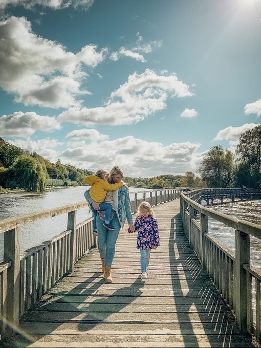 Family crossing a wooden walkway over the river in the sunshine