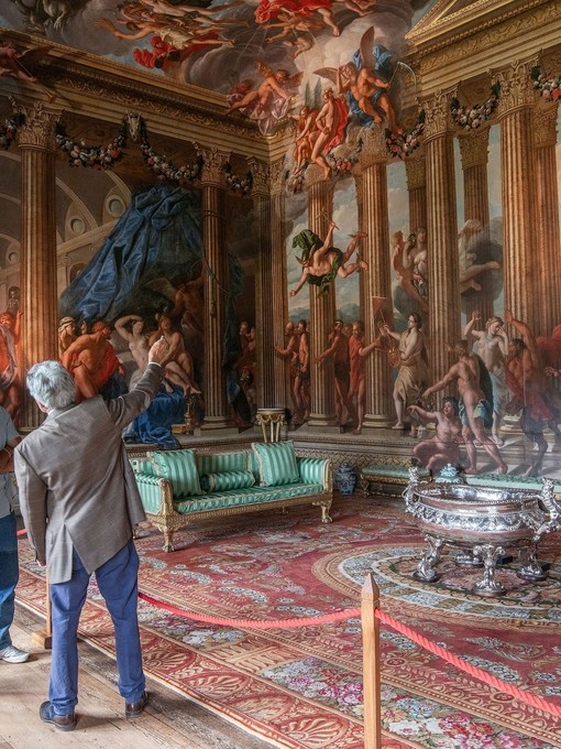 A man and a woman with a tour guide in an ornate room with paintings