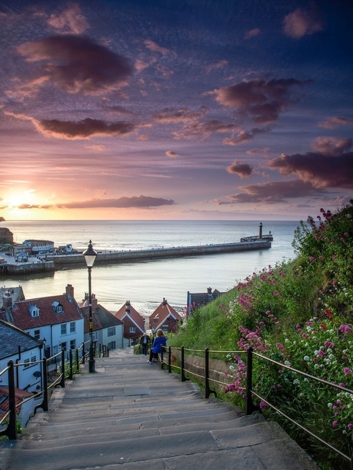 Two people on the steps of a hillside looking towards the pier