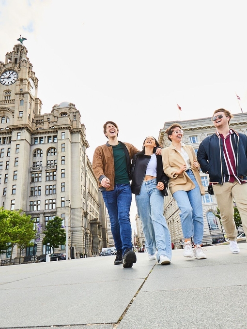 Four friends exploring a local city walking along waterfront promenade, with historic buildings in the background