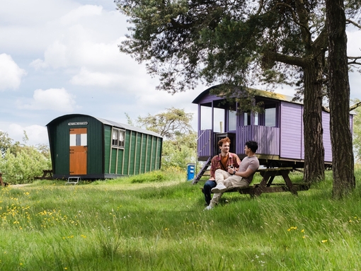 Two men sat oustide a shepherds hut in the countryside