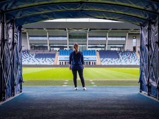 Woman standing in front of the pitch at the Manchester City Academy Stadium