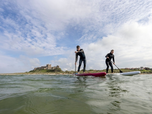 Two men on are paddleboarding in the sea with a heritage castle in the background.