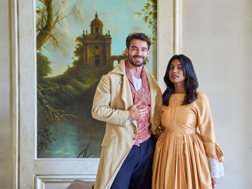 Ein Mann und eine eine Frau, die in historischen Kostümen gekleidet, lächeln in die Kamera