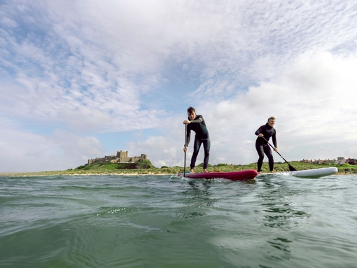 Two men on are paddleboarding in the sea with a heritage castle in the background.