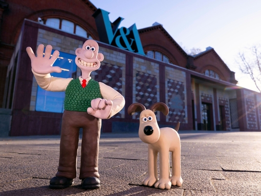 A clay character of a man waving outside a museum alongside a clay dog