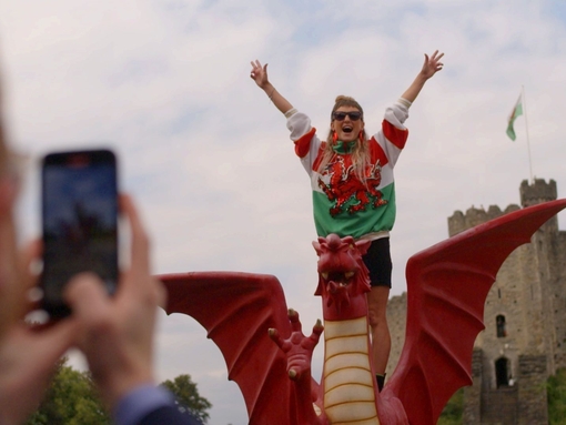 Woman has picture taken standing on a model Welsh dragon.